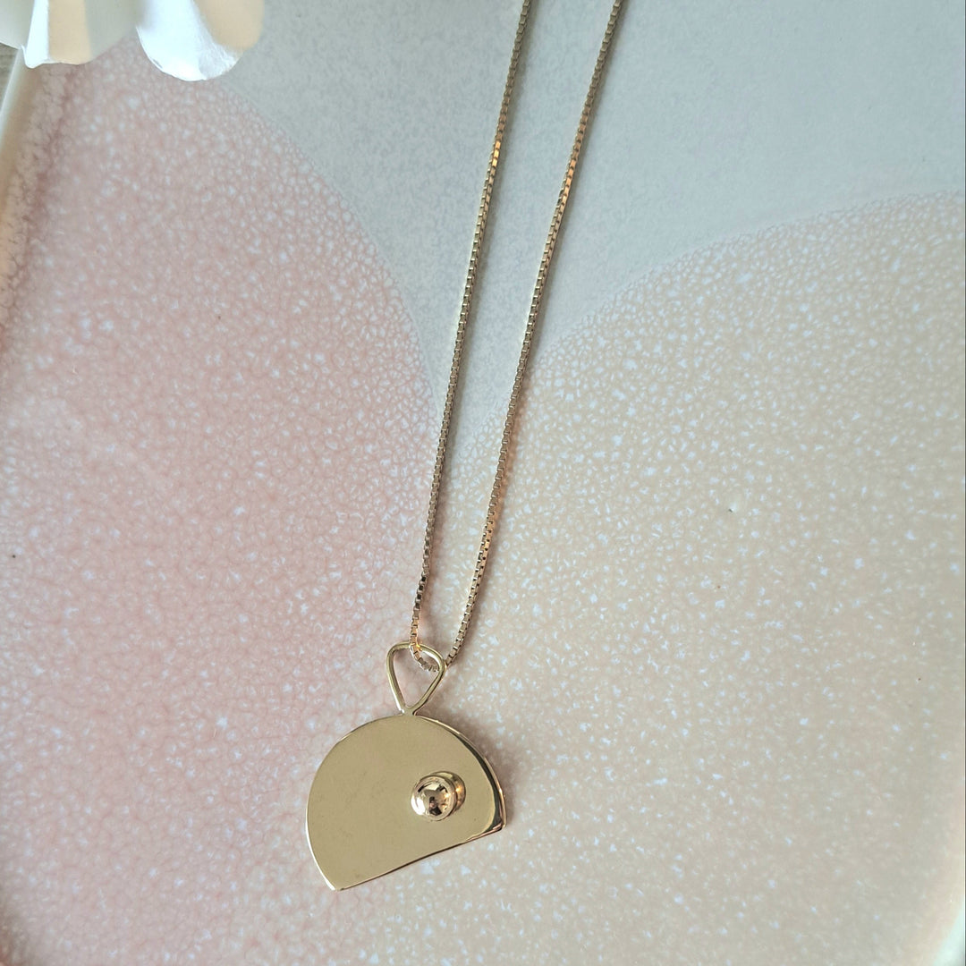 Gold necklace by Bold Lines Jewellery with a cut disc shaped pendant on a pink and white background