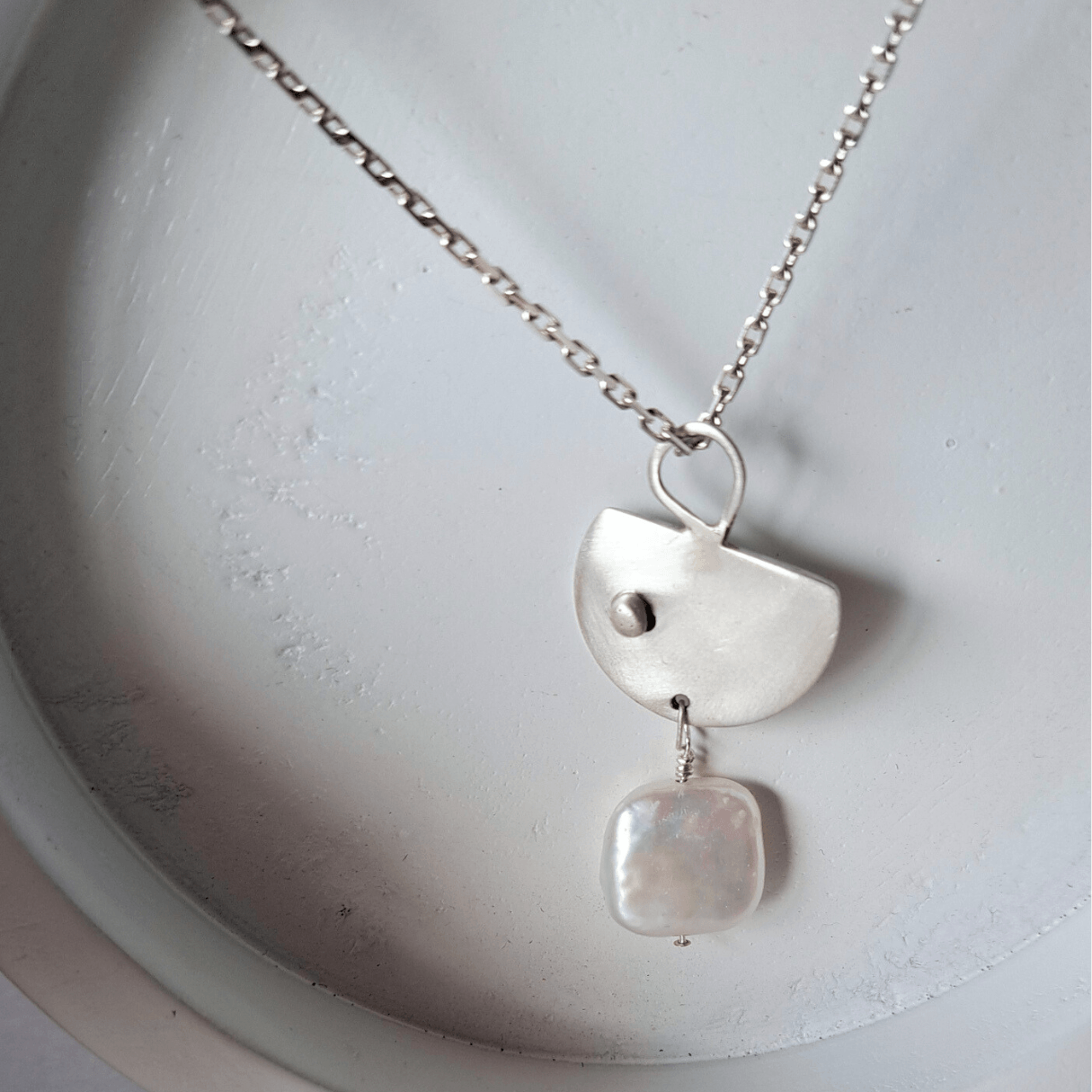 Silver necklace with two pendant charms on a white dish