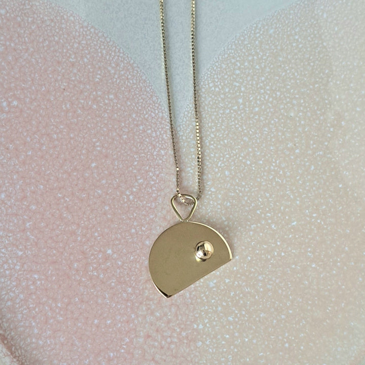 Gold plating or brass necklace with a cut disc shaped pendant on a pink and white textured surface.