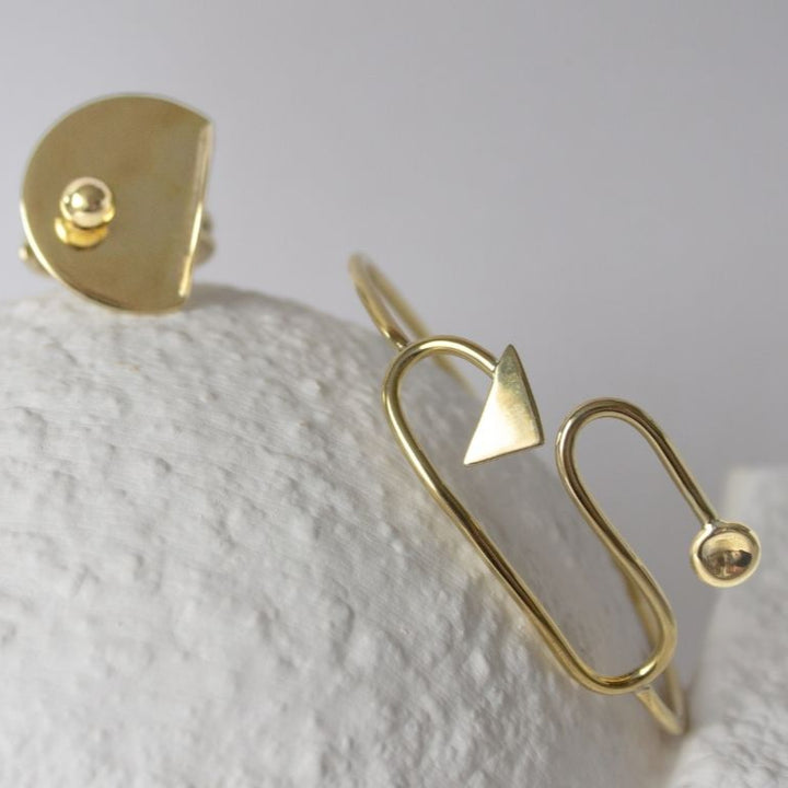Gold earring with geometric design on a textured white surface
