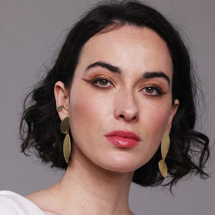 Woman wearing gold fluidity earrings bold Lines against a gray background
