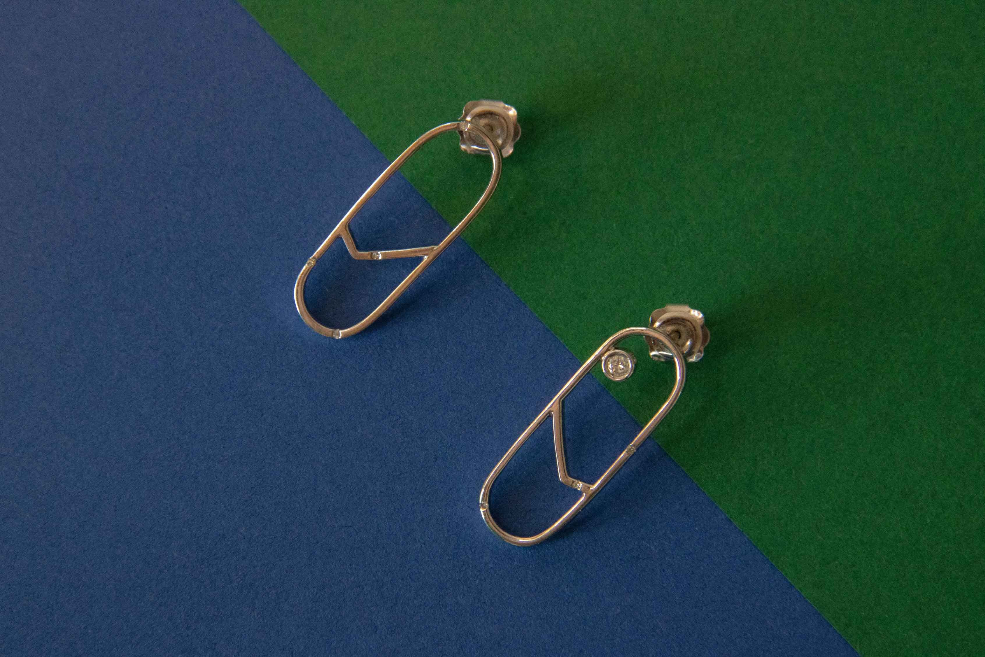 Geometric minimal 9ct white gold earrings with diamonds designed by Bold Lines Jewellery shown on a green and blue background.