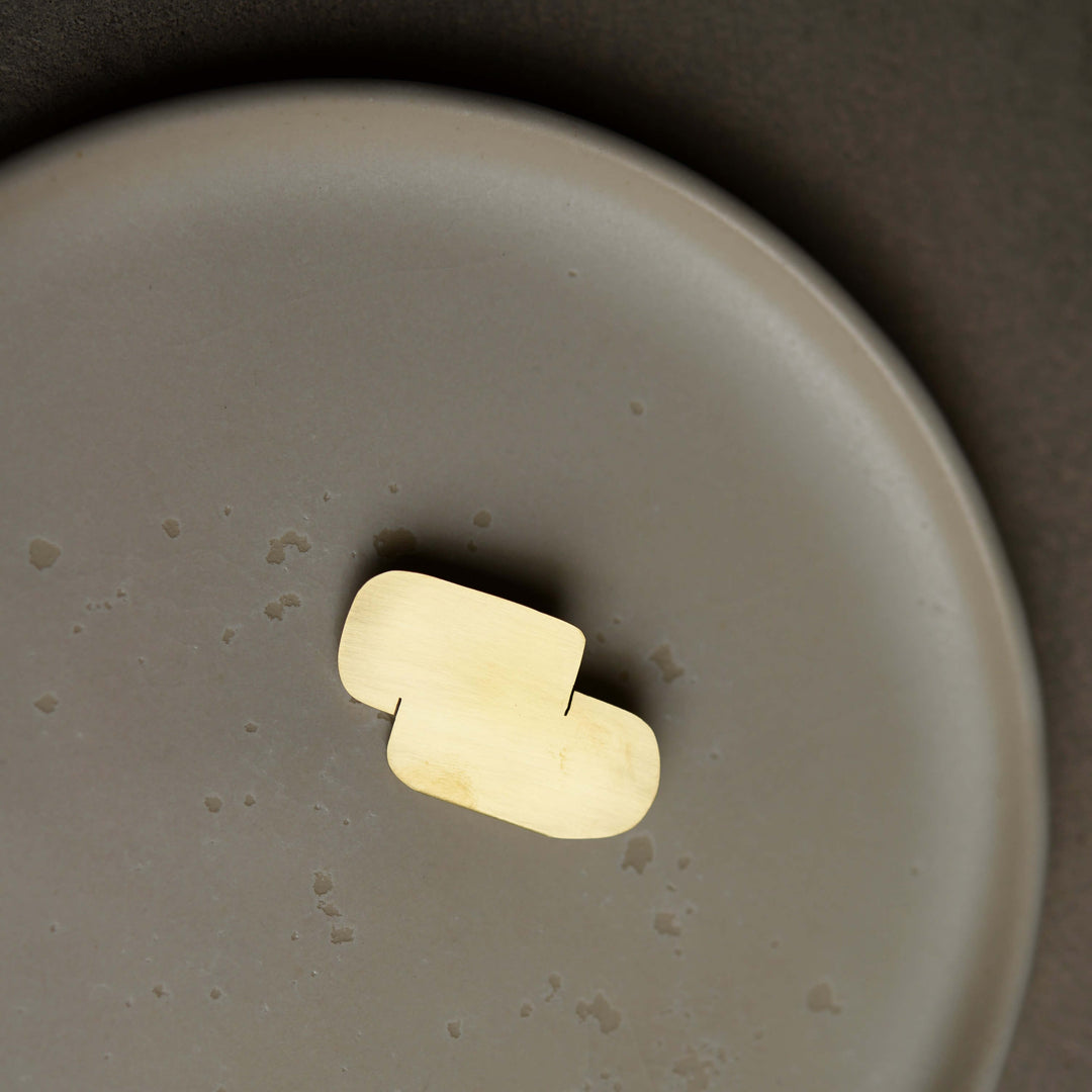 Gold Bold Lines jewellery Connection modern Brooch on a ceramic beige plate.