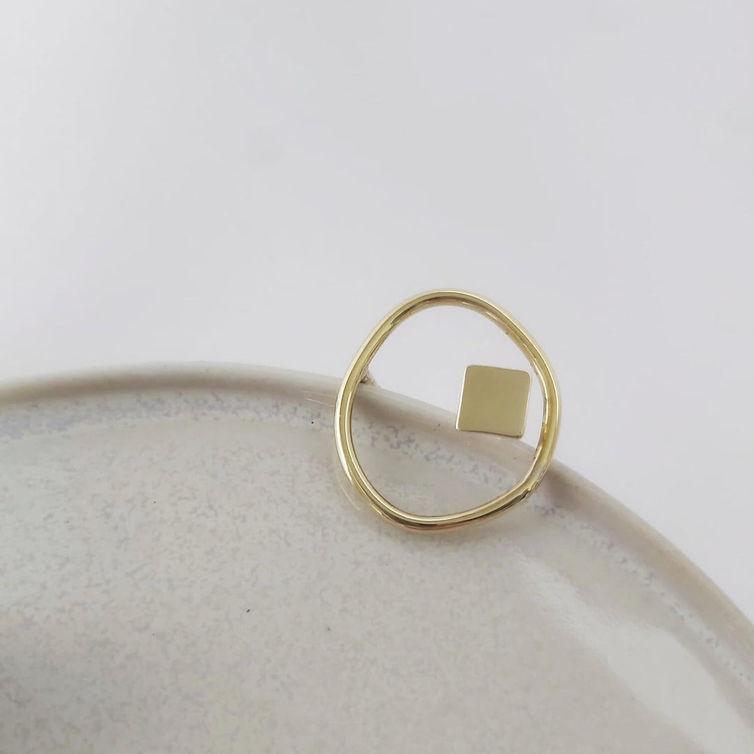 geometric and organic gold ring set on a ceramic plate.