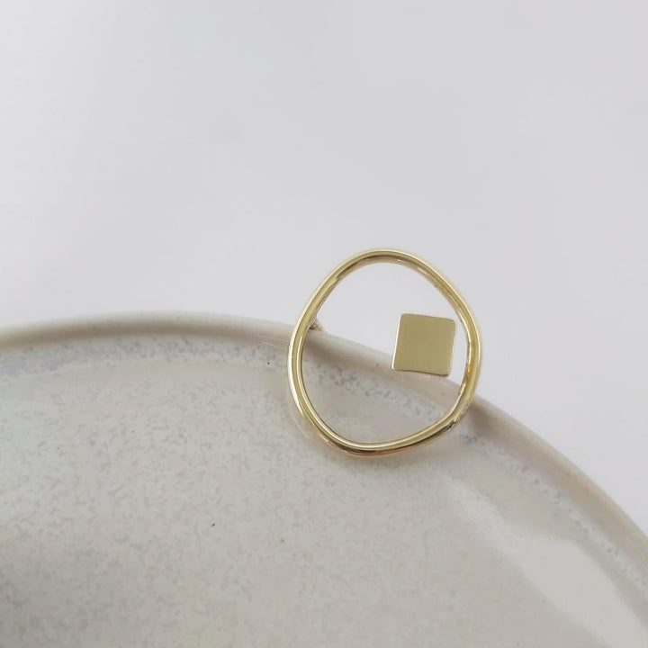 geometric and organic gold ring set on a ceramic plate.