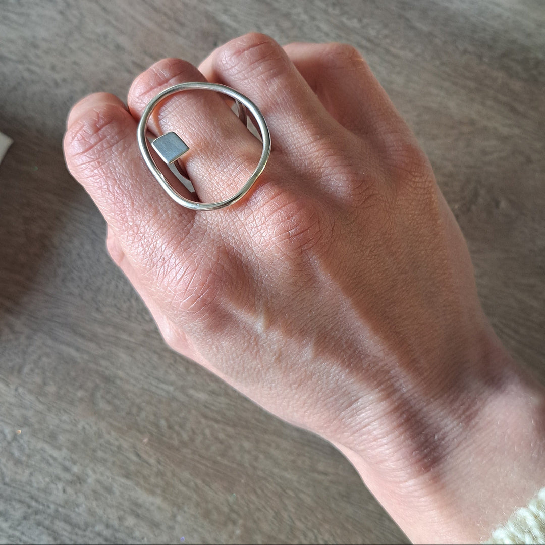 Hand wearing a bold lines jewellery silver ring on a wooden surface with jewellery boxes in the background