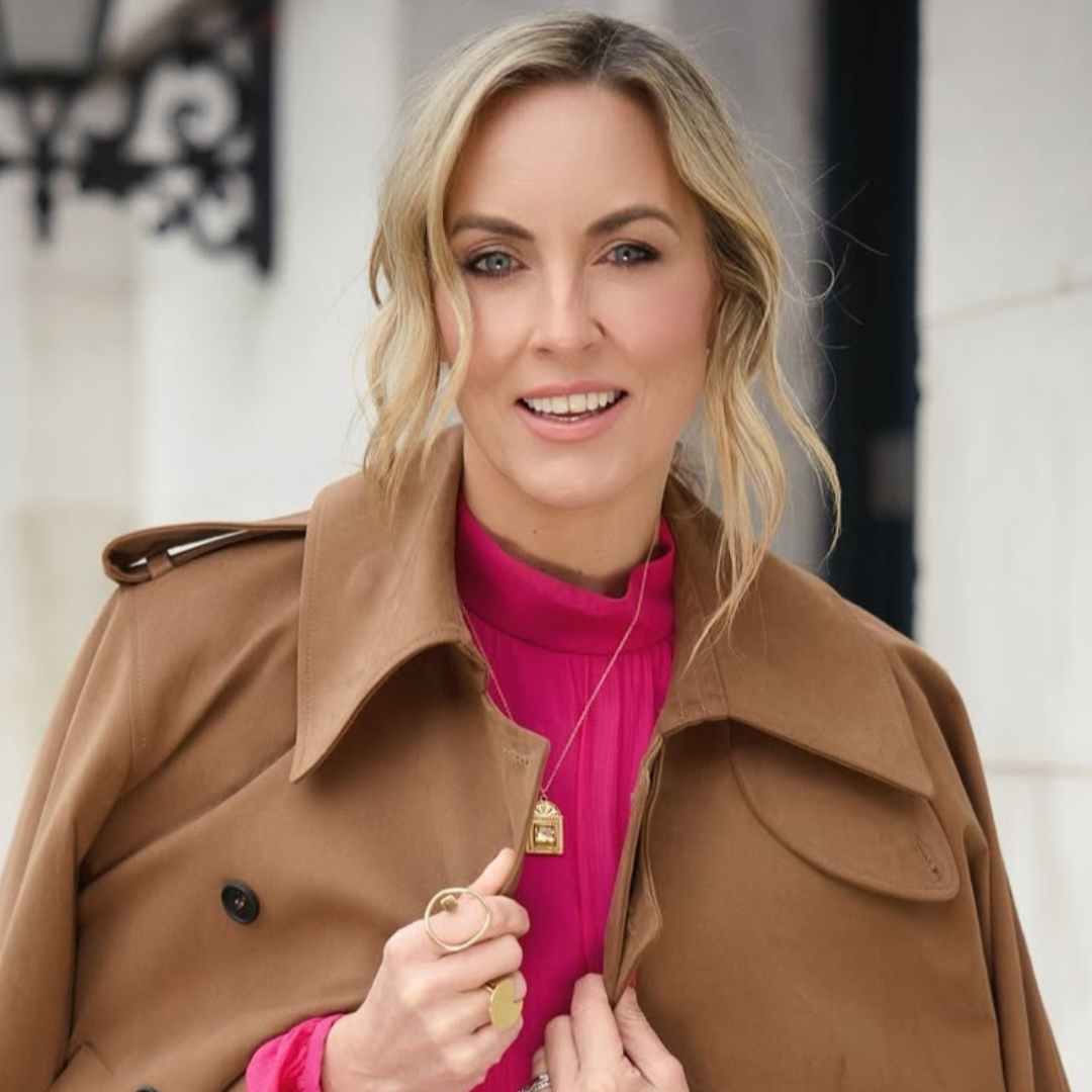Woman wearing a brown coat over a pink outfit with a blurred background