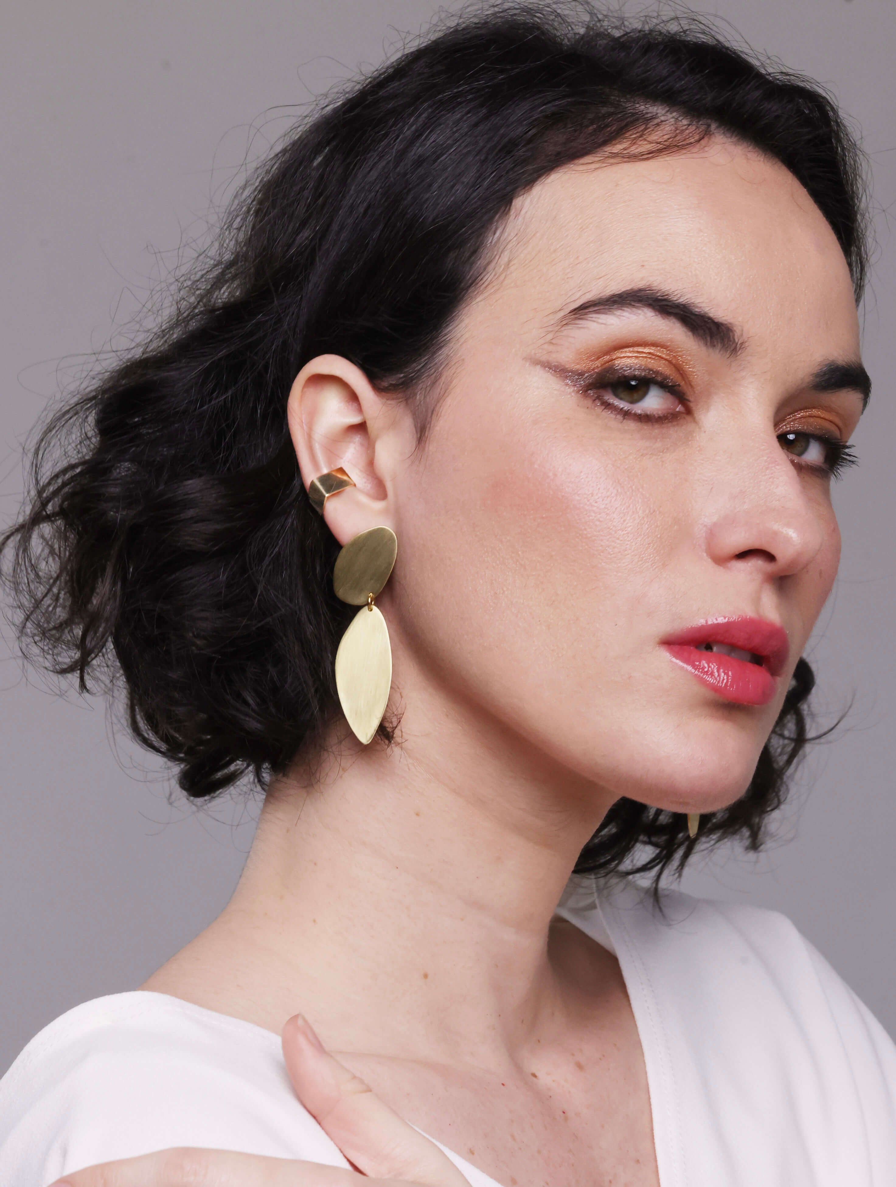 Woman wearing gold earrings and ring against a neutral background