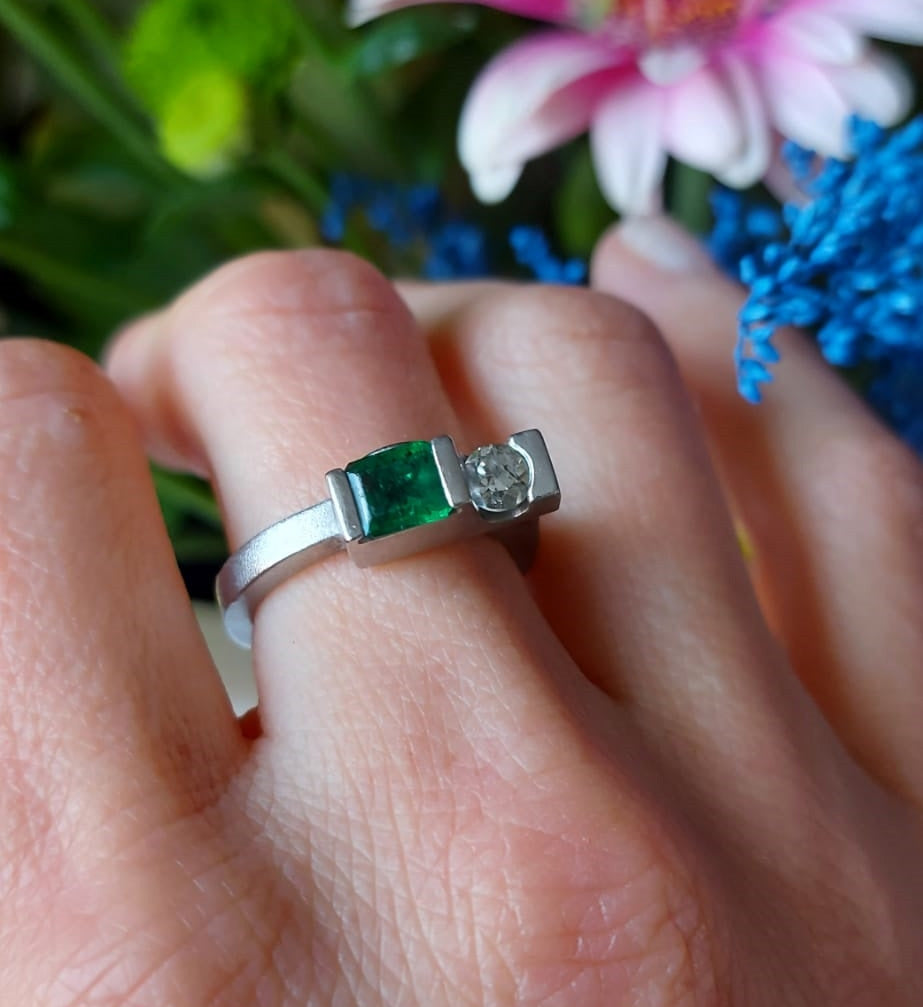 Contemporary emerald and diamonds palladium remodelled ring designed by Bold Lines jewellery shown in front of a floral background.