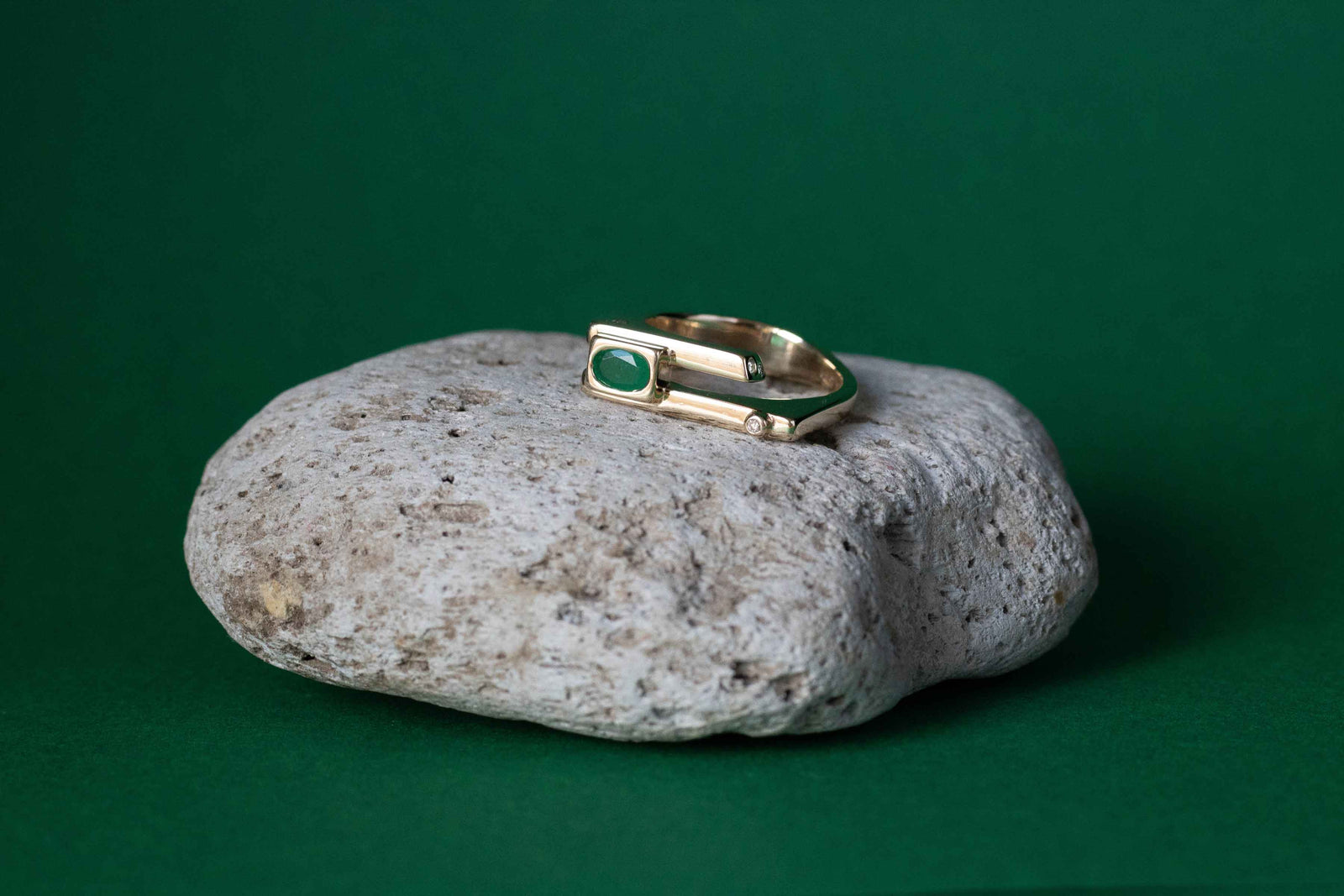 Contemporary emerald 18ct yellow gold and diamonds remodelled ring shown on a natural stone in front of a green backdrop.