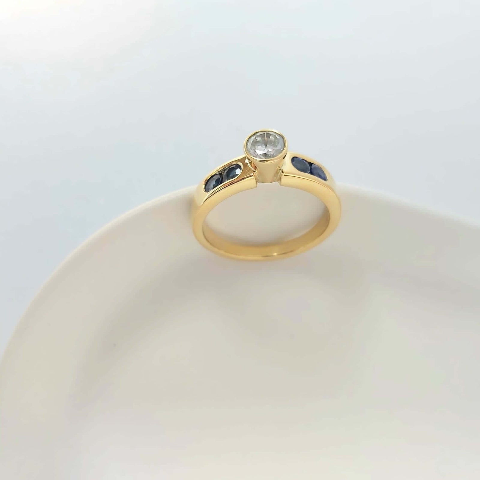Modern yellow gold, sapphires and diamonds remodelled ring designed by Bold Lines jewellery shown on a white ceramic plate. 