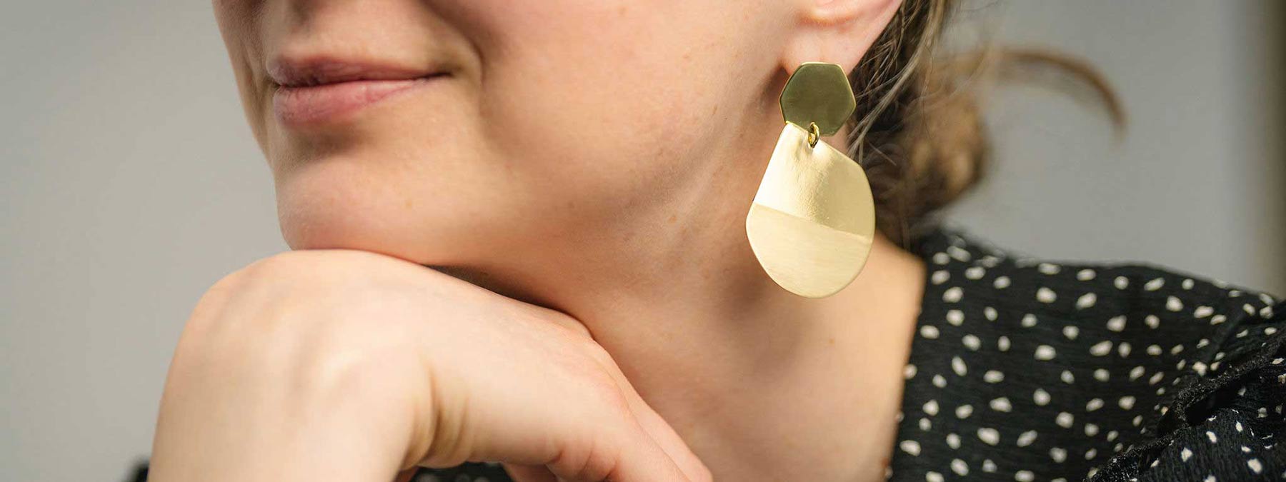 Bold Lines Jewellery Reflection gold earrings and balance bracelet worn on a model wearing a black polka dots top.