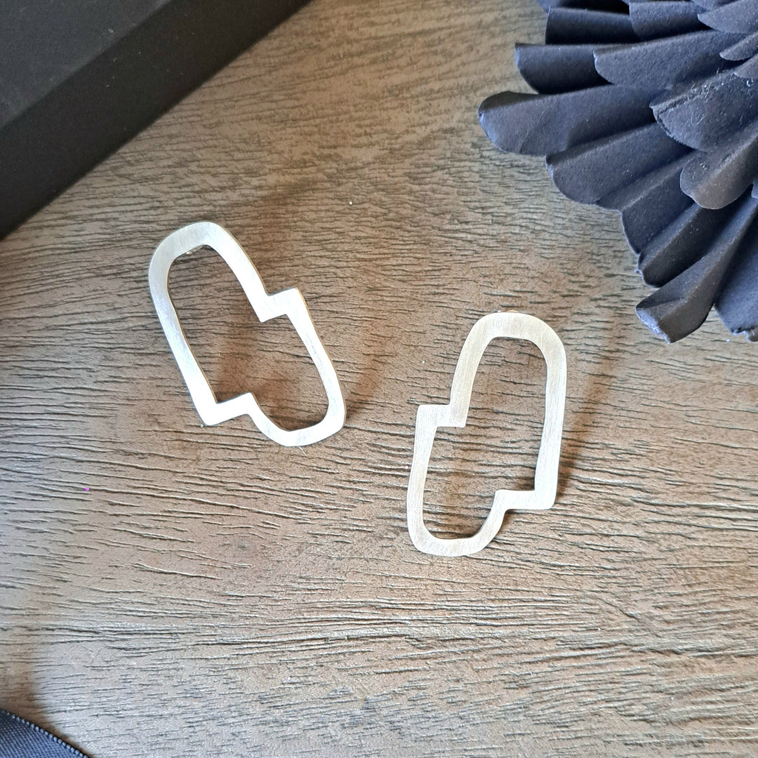 Sterling silver Connection II earrings on a wooden surface with a black box and gray textured object in the background.