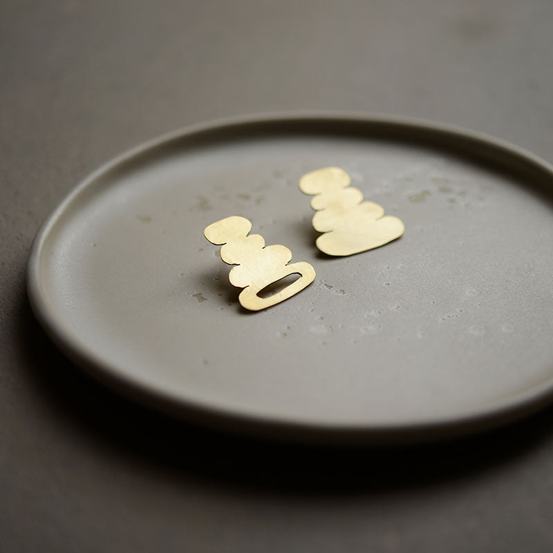 Organic-shaped brass stud earrings with sterling silver backs lying on a grey ceramic plate.