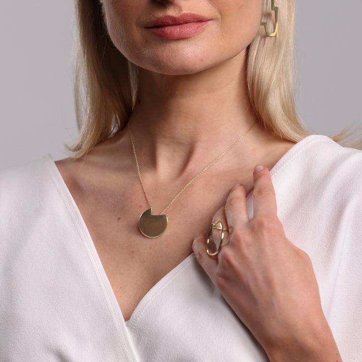 Woman wearing gold jewelry including earrings, necklace, and ring against a neutral background