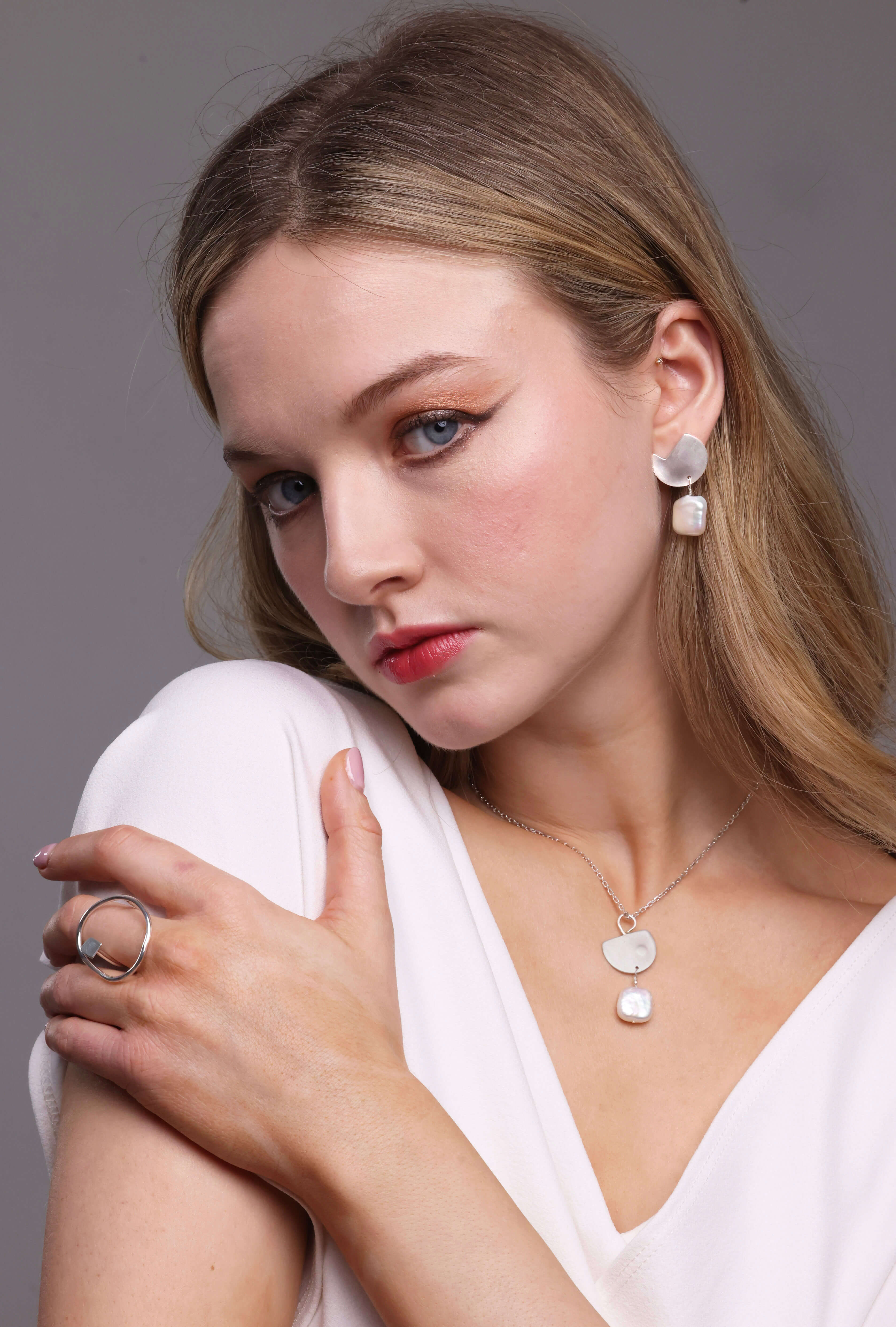 Woman wearing a pearl necklace in sterling silver by bold LINES jewelllery with a plain background