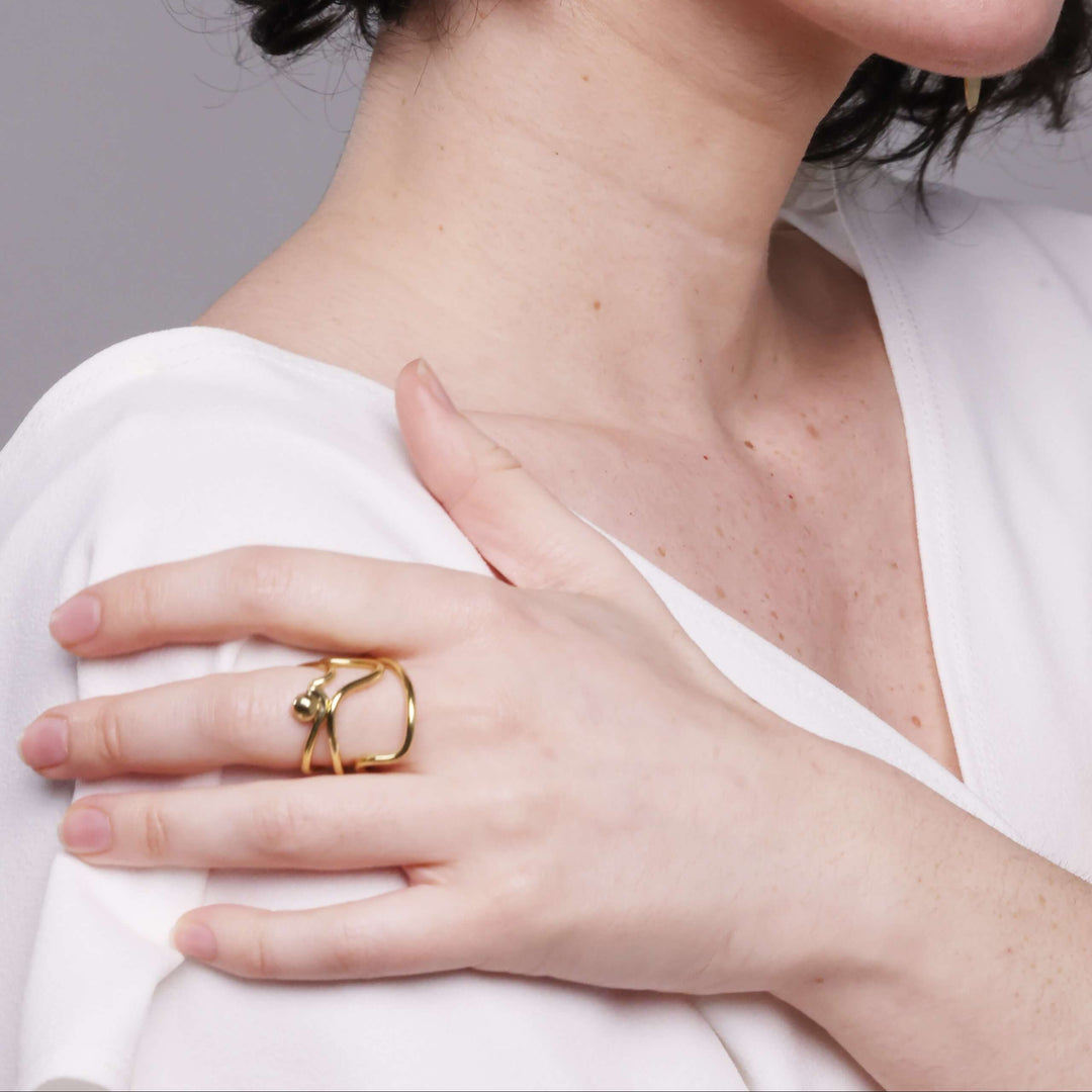 Woman wearing a gold ring by bold lines jewellery on her hand with a neutral background