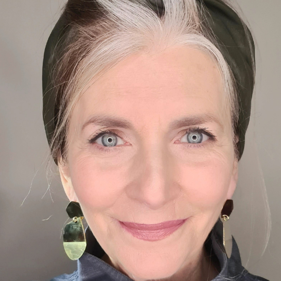 Woman with gray hair wearing a headband against a neutral background