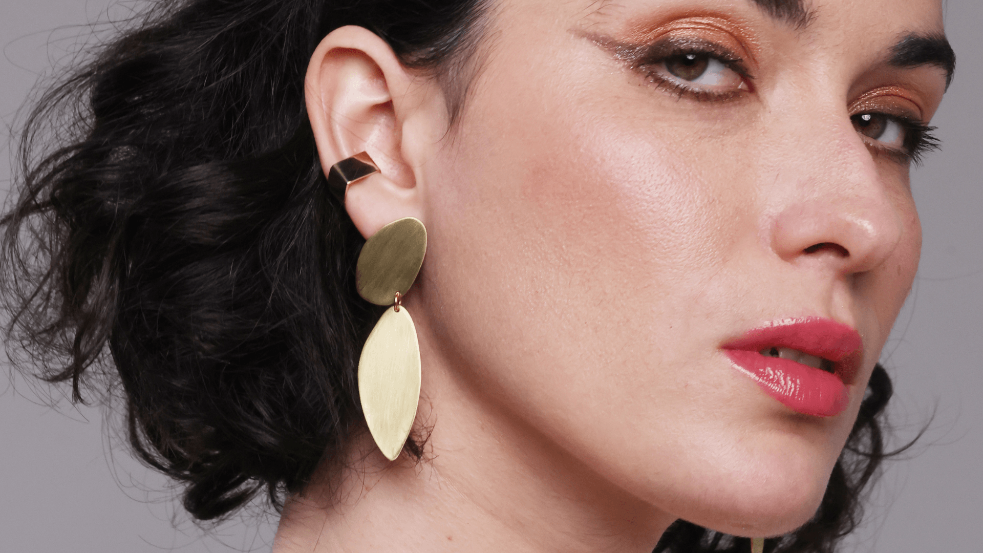 Close-up of a woman wearing gold earrings with a neutral background