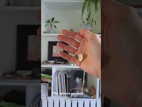 Video of a hand holding the gold abstract Balance necklace in front of shelves.