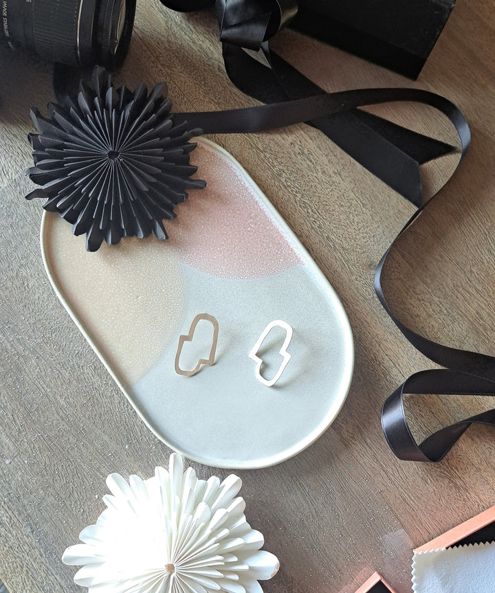Black decorative item on a white dish with sterling silver Connection II earrings, surrounded by ribbons on a wooden surface.