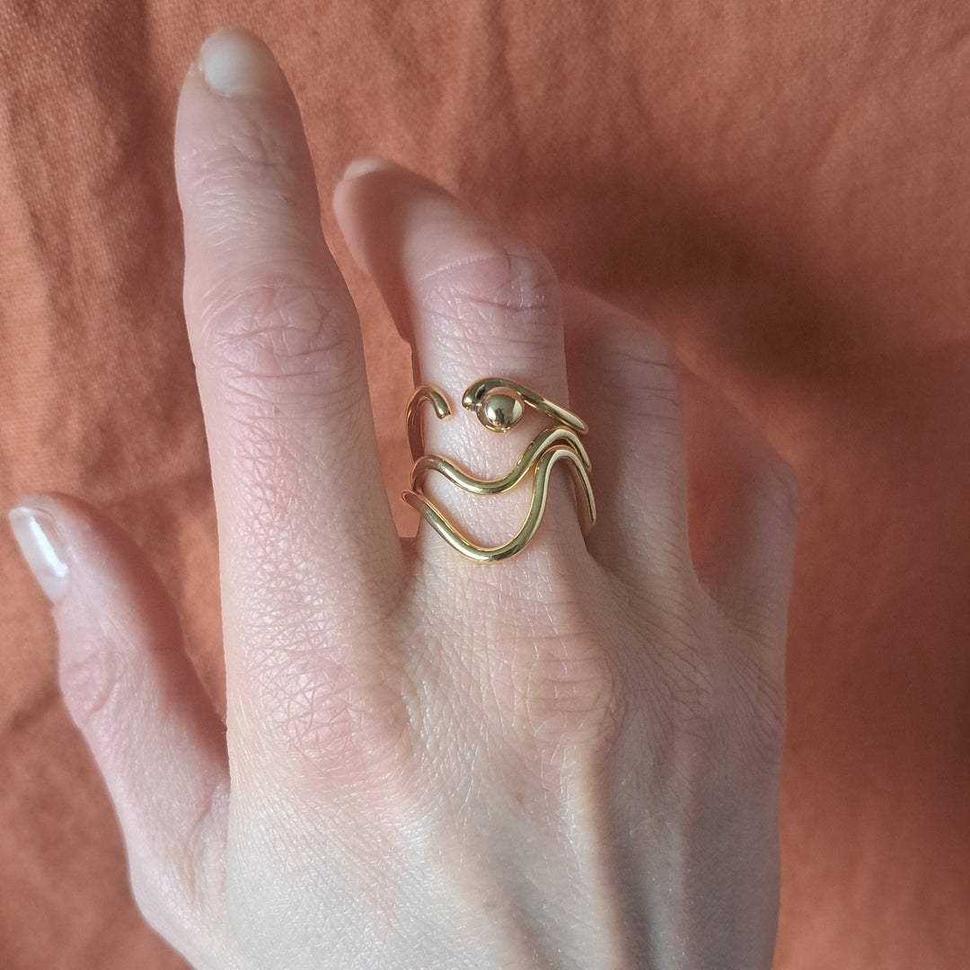 Gold ring on a person's finger against a soft pink background