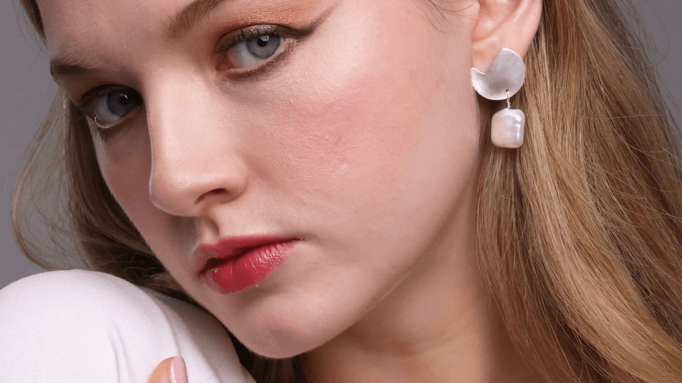 Close-up of a woman wearing pearl earrings with a neutral background