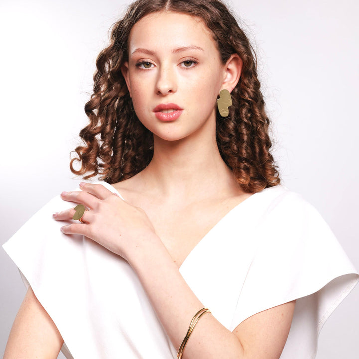 Woman wearing a white top with bold lines jewellery  gold jewelry against a light background