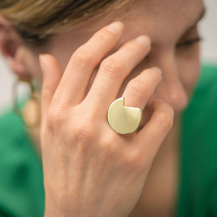 Close-up of a hand wearing a gold plated abstract ring with a green shirt in the background